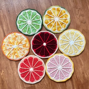 May include: Seven crocheted coasters in the shape of citrus fruit slices. The coasters are in shades of green, yellow, orange, red, and pink.