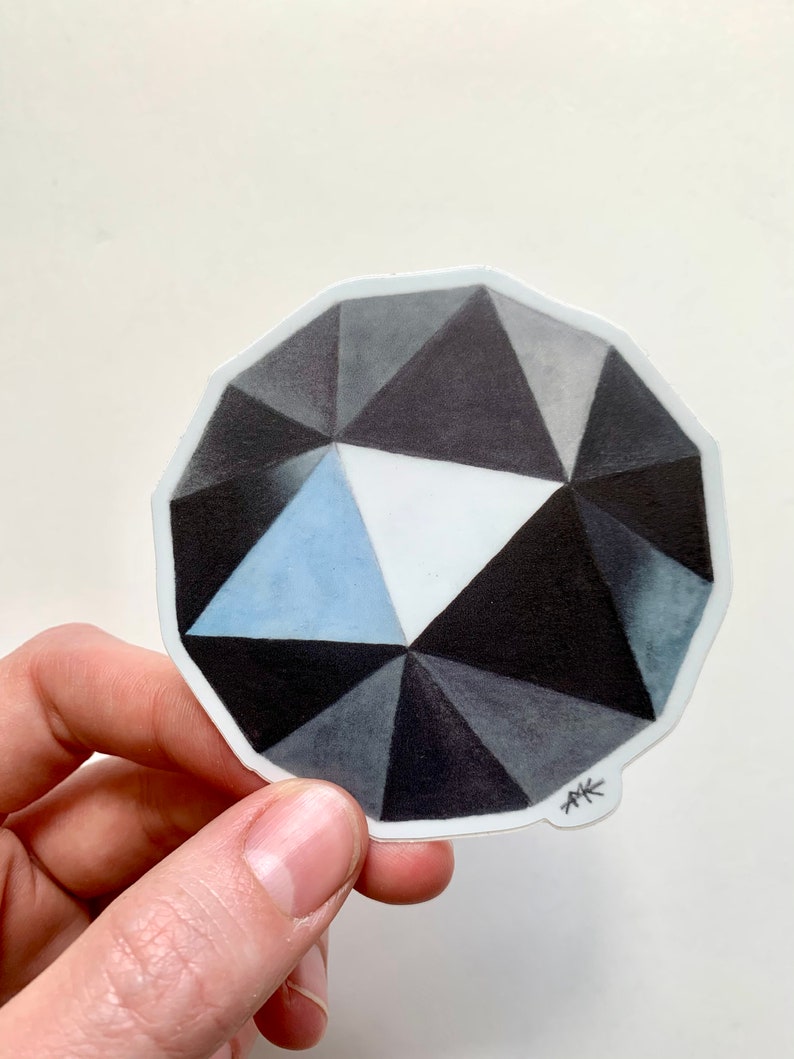 May include: A black and white geometric sticker of a diamond with a blue center. The sticker has a white border and the artist's initials "AK" are in the bottom right corner.
