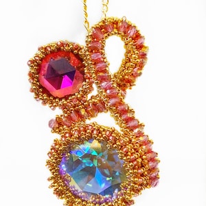 May include: A gold chain necklace with a pendant featuring two large faceted crystals, one pink and one iridescent, surrounded by gold and pink beads.
