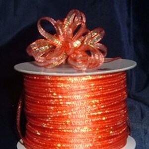 May include: A spool of orange iridescent ribbon with a matching bow on top. The ribbon is wound tightly on the spool and has a shiny, metallic finish.