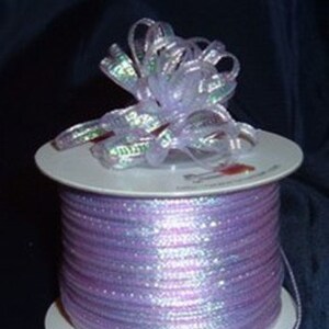 May include: A spool of iridescent lavender ribbon with a matching bow. The ribbon is wrapped around a white spool with a label.