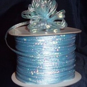 May include: A spool of light blue iridescent ribbon with a matching bow on top. The ribbon is wound around a white plastic spool.