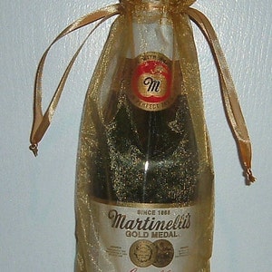 May include: A gold mesh gift bag with a clear glass bottle of Martinelli's Gold Medal Sparkling Cider. The bottle label features the brand name, "Martinelli's Gold Medal", and the words "Sparkling Cider". The bottle is 25.4 fluid ounces (1.6 pints) and contains no alcohol.