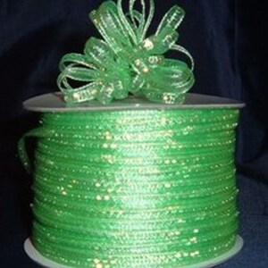 May include: A spool of green iridescent ribbon with a matching bow. The ribbon is wrapped around a white spool.