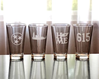 May include: Four clear glass pint glasses with different designs etched on them. The designs include a star, a city skyline, the word "HOME" with a heart, and the number "615".