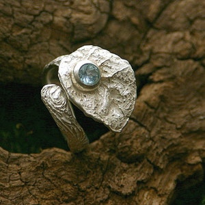 Può includere: Un anello d'argento con un design a foglia testurizzato e una pietra preziosa blu chiaro.