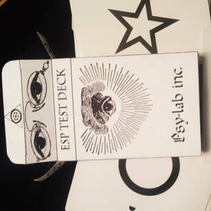 May include: A white box with black text that reads "ESP Test Deck" and "Psy-Lab inc." The box features a black and white illustration of an eye with rays of light emanating from it.