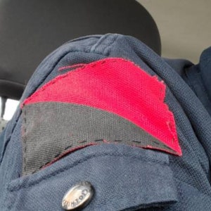 May include: A dark blue jacket with a red and black patch sewn on the left shoulder. The patch is a diagonal split of red and black fabric.