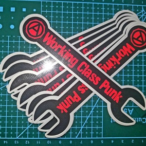 May include: Five black and silver wrench stickers with the text "Working Class Punk" in red letters. The stickers are stacked on top of each other and have a red anarchy symbol in the top corner.
