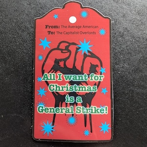 May include: Red tag with the text "From: The Average American To: The Capitalist Overlords." The tag features a black fist graphic and the words "All I want for Christmas is a General Strike!" in green.
