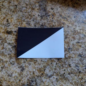 May include: A black and white square sticker with a diagonal line dividing the two colors.