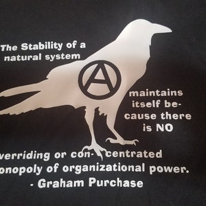 May include: Black t-shirt with a white silhouette of a raven with an anarchy symbol inside its body. The text reads "The Stability of a natural system maintains itself because there is NO overriding or concentrated monopoly of organizational power. - Graham Purchase"