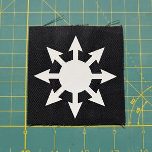 May include: Black fabric patch with a white eight-pointed star design. The star has eight arrows pointing outwards from the center.