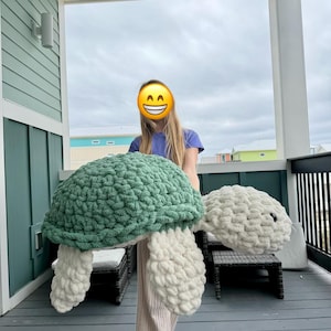 May include: A large, handmade crochet turtle in shades of green and white. The turtle has a textured shell and large, fluffy flippers. The turtle is a soft, plush toy.