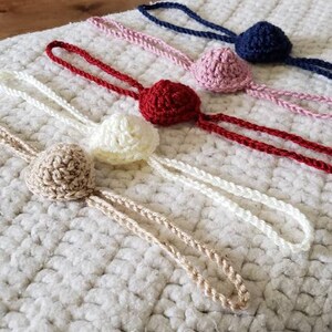 May include: Five crocheted headbands with different colored balls on the end. The headbands are white, beige, red, pink, and blue.