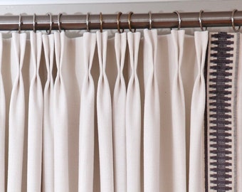 May include: White linen curtains with a brown and white patterned trim. The curtains are hung on a silver curtain rod with decorative finials.