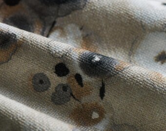 May include: Close-up of a beige fabric with a textured surface. The fabric has a pattern of abstract shapes in shades of brown, black, and white.