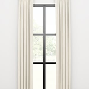 May include: A pair of off-white curtains with pleats hanging from a gold rod in front of a window with black trim.