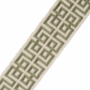 May include: A white fabric trim with a green geometric pattern. The pattern is a repeating design of squares and rectangles.