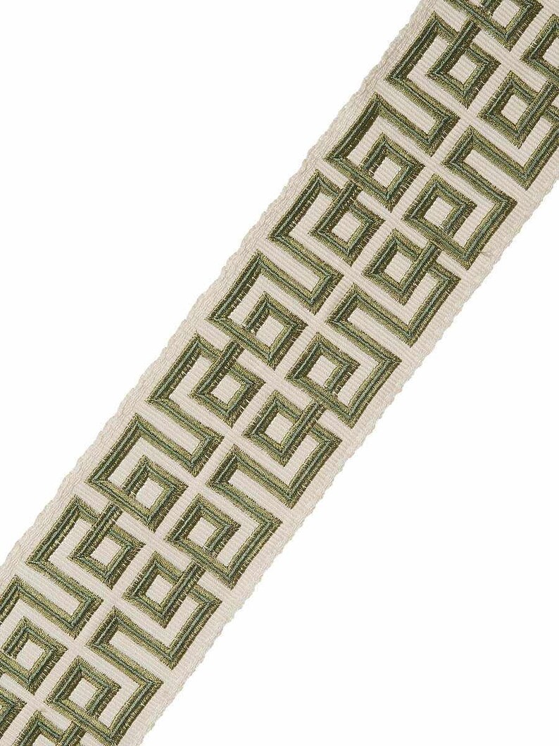 May include: A white fabric trim with a green geometric pattern. The pattern is a repeating design of squares and rectangles.
