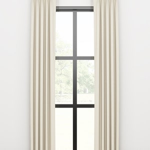 May include: A pair of off-white curtains with pleats hanging from a gold curtain rod in front of a window with black trim.