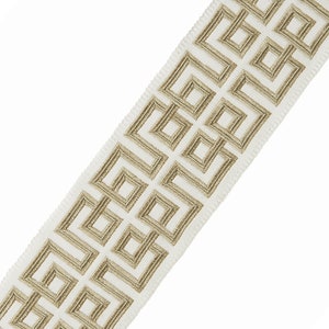 May include: White fabric trim with a gold geometric pattern. The pattern is a repeating design of squares and rectangles.