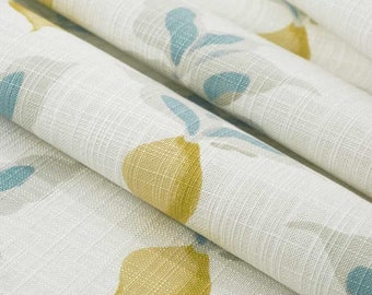 May include: Close-up of a white fabric with a repeating pattern of yellow lemons and blue leaves. The fabric has a subtle texture.