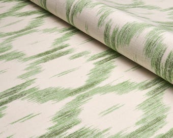 May include: Close-up of a white fabric with a green ikat pattern. The fabric is folded in half, showing the pattern on both sides.