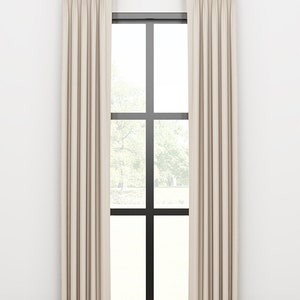 May include: A pair of off-white curtains with pleats hanging from a gold curtain rod in front of a window with black trim.