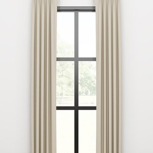 May include: A pair of off-white curtains with pleats hanging from a gold curtain rod in front of a window with black trim.