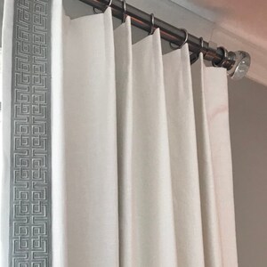 May include: White curtains with a gray geometric pattern border hanging from a silver curtain rod.
