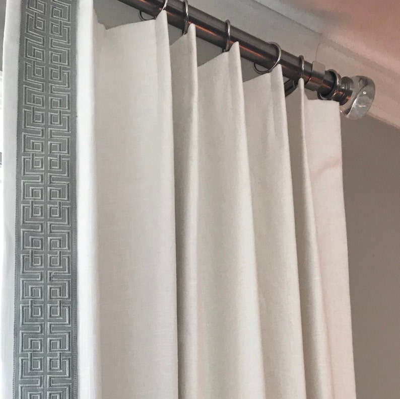 May include: White curtains with a gray geometric pattern border hanging from a silver curtain rod.