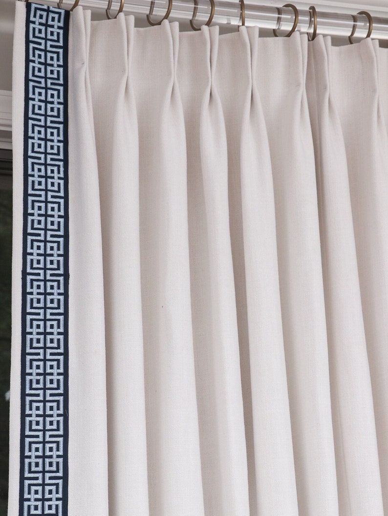 May include: White curtains with a geometric pattern border in blue and white. The curtains are pleated and hung on a clear rod.