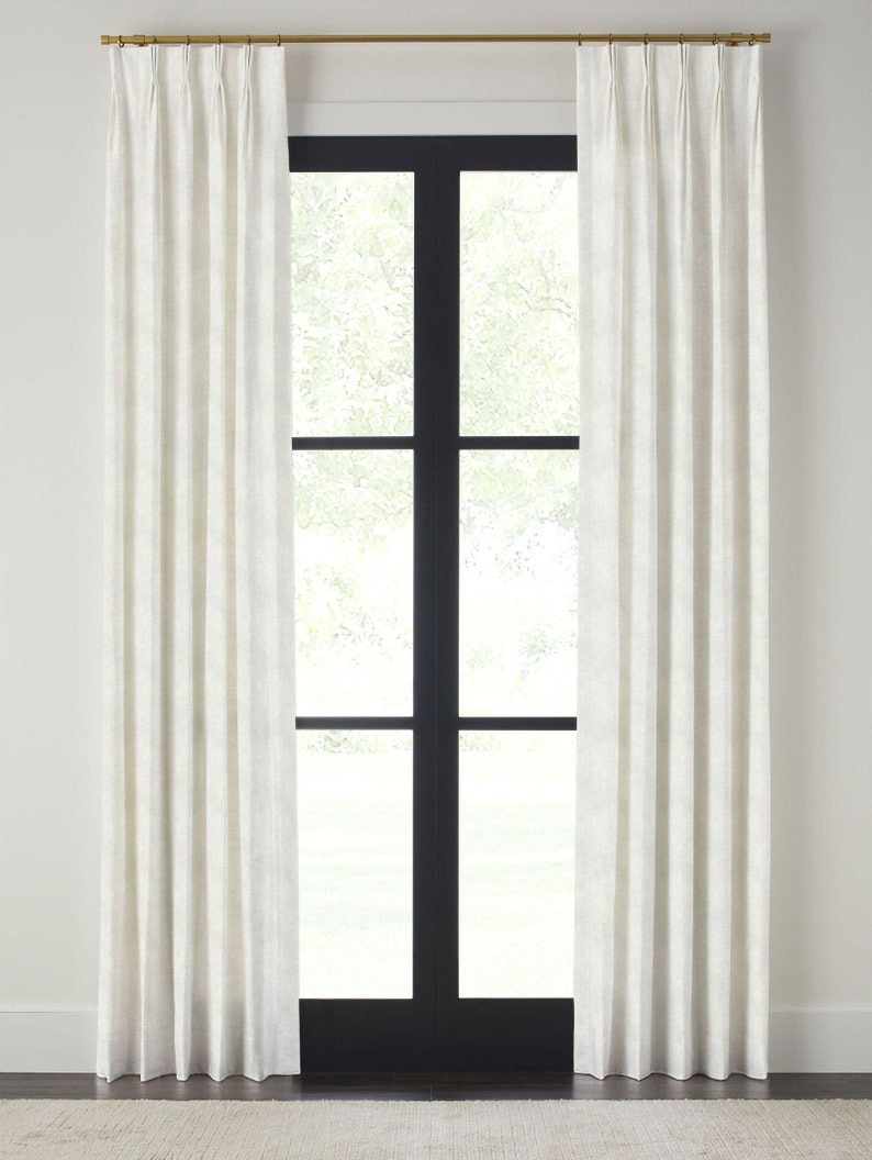 May include: White linen curtains with pleats hanging from a gold rod in front of a black framed window. The curtains are drawn and the window is closed.