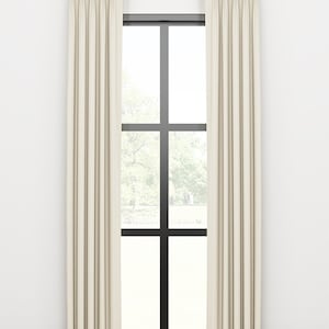 May include: A pair of off-white curtains with pleats hanging from a gold curtain rod in front of a window with black trim.