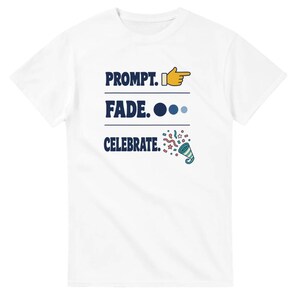 May include: A white short-sleeved t-shirt featuring dark blue text that reads PROMPT. FADE. CELEBRATE. The design includes a yellow pointing finger emoji next to PROMPT, three blue circles next to FADE, and a colorful party popper icon next to CELEBRATE.