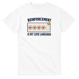 Può includere: Una t-shirt bianca a maniche corte con una grafica che riporta il testo REINFORCEMENT IS MY LOVE LANGUAGE in blu scuro. Il design include un riquadro rettangolare contenente quattro cuori rossi e un cerchio vuoto tratteggiato con una stella gialla.