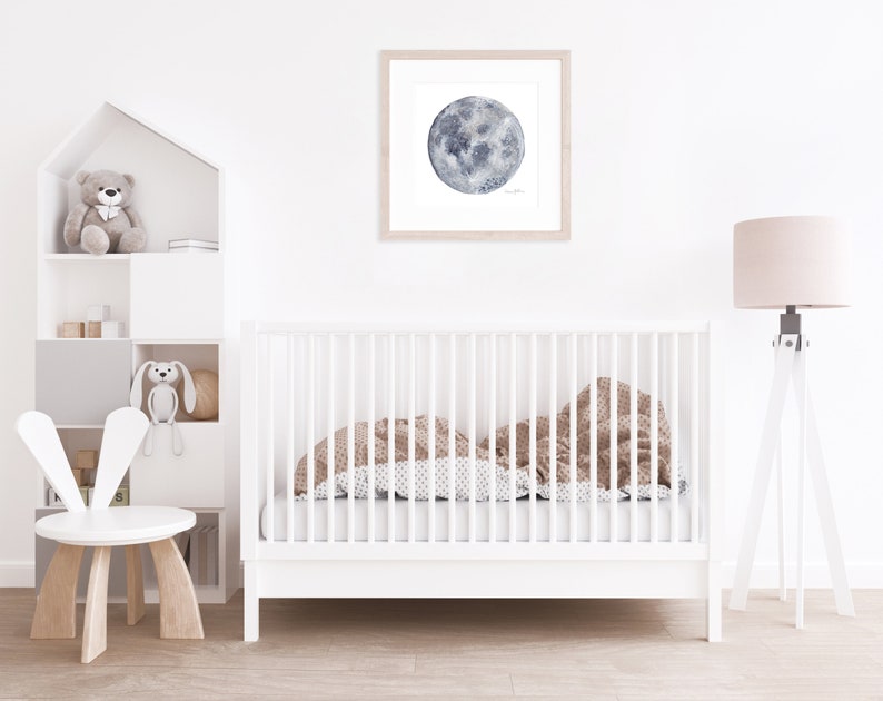 K&ouml;nnte beinhalten: Ein wei&szlig;es Babybett mit einer braunen und wei&szlig;en gemusterten Decke im Inneren. Ein wei&szlig;er Hasenstuhl steht im Vordergrund. Ein wei&szlig;es Regal mit einem Teddyb&auml;r und einem Hasenspielzeug befindet sich im Hintergrund. Ein gerahmtes Aquarellbild eines Mondes h&auml;ngt an der Wand. Eine wei&szlig;e Stehlampe mit einem beigefarbenen Lampenschirm steht in der Ecke.
