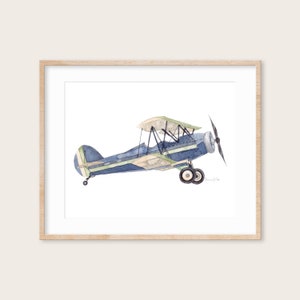 Puede incluir: Una pintura de acuarela de un biplano azul y verde sobre un fondo blanco. El avi&oacute;n est&aacute; en vuelo y tiene una h&eacute;lice en la parte delantera.
