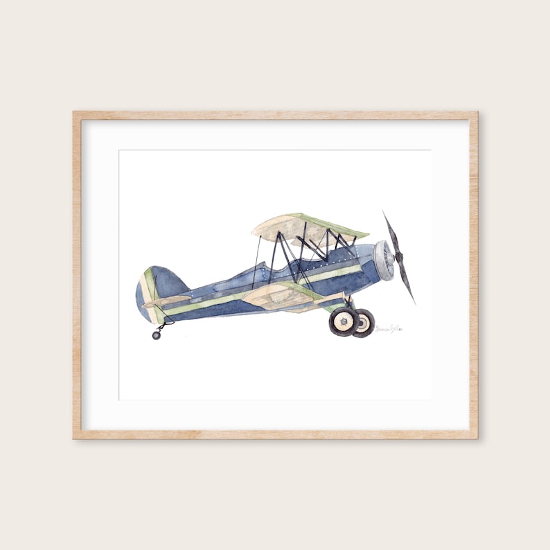 Puede incluir: Una pintura de acuarela de un biplano azul y verde sobre un fondo blanco. El avi&oacute;n est&aacute; en vuelo y tiene una h&eacute;lice en la parte delantera.