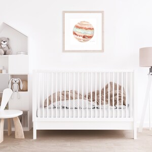 Peut inclure: Une impression encadr&eacute;e &agrave; l'aquarelle de la plan&egrave;te Jupiter, avec des bandes orange, rouge et sarcelle. L'&oelig;uvre est accroch&eacute;e au-dessus d'un lit b&eacute;b&eacute; blanc avec une couverture &agrave; motifs. Une chaise blanche et une &eacute;tag&egrave;re avec des jouets sont &eacute;galement dans la pi&egrave;ce.