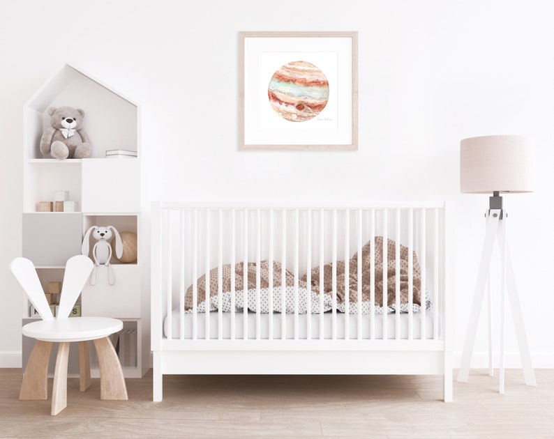 Peut inclure: Une impression encadr&eacute;e &agrave; l'aquarelle de la plan&egrave;te Jupiter, avec des bandes orange, rouge et sarcelle. L'&oelig;uvre est accroch&eacute;e au-dessus d'un lit b&eacute;b&eacute; blanc avec une couverture &agrave; motifs. Une chaise blanche et une &eacute;tag&egrave;re avec des jouets sont &eacute;galement dans la pi&egrave;ce.
