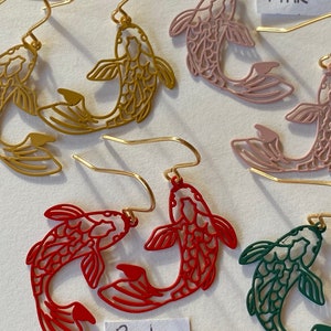 K&ouml;nnte beinhalten: Ein Set mit f&uuml;nf Paaren goldfarbener fischf&ouml;rmiger Ohrringe. Die Ohrringe sind in Rot, Rosa, Gr&uuml;n und Gold erh&auml;ltlich. Die Ohrringe sind mit "Rot", "Rosa" und "Gold" beschriftet.