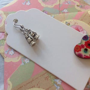 May include: A pair of silver earrings shaped like lanterns hanging from a white tag with a floral patterned envelope behind it.