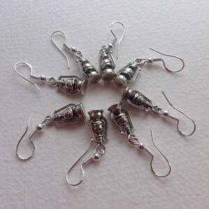 May include: Eight silver dangle earrings with a lantern charm. Each earring has a silver hook and a small silver ball at the end of the hook.