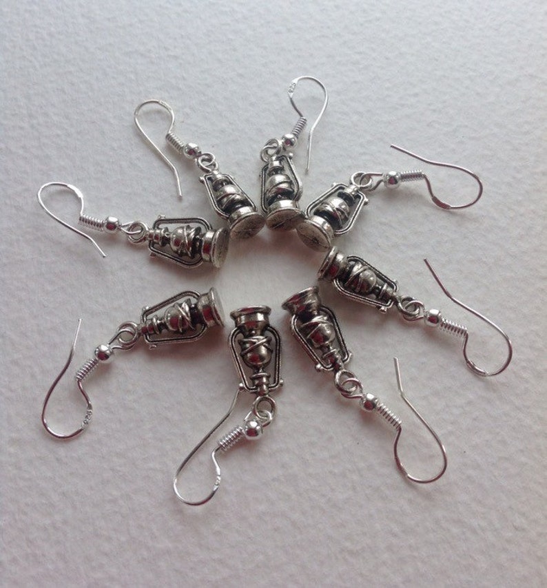 May include: Eight silver dangle earrings with a lantern charm. Each earring has a silver hook and a small silver ball at the end of the hook.