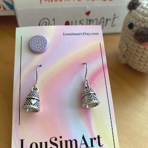 Puede incluir: Un par de pendientes de dedal de plata con un pequeño dije de corazón en cada dedal. Los pendientes se muestran en una tarjeta blanca con el texto "LouSimArt" y "Made with love for you".