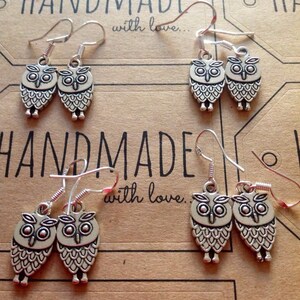 Pode incluir: Tr&ecirc;s pares de brincos de prata com formato de coruja com fecho de gancho. Os brincos s&atilde;o feitos &agrave; m&atilde;o e apresentam o texto "Handmade with love." no fundo.