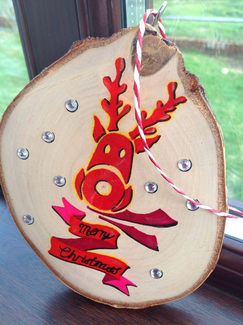 May include: A wooden Christmas ornament with a red reindeer design and the words "Merry Christmas" in pink lettering. The ornament is decorated with rhinestones.