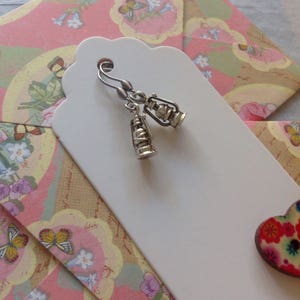 May include: Silver dangle earrings with a lantern charm. The earrings are displayed on a white tag with a pink and green floral pattern.